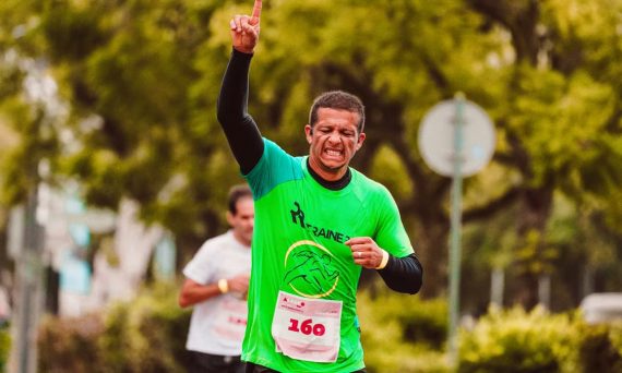 Joyful male runner celebrates a marathon win outdoors, raising arms in triumph.