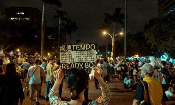 Crowd gathered in Taipei for a demonstration at night with urban cityscape backdrop.